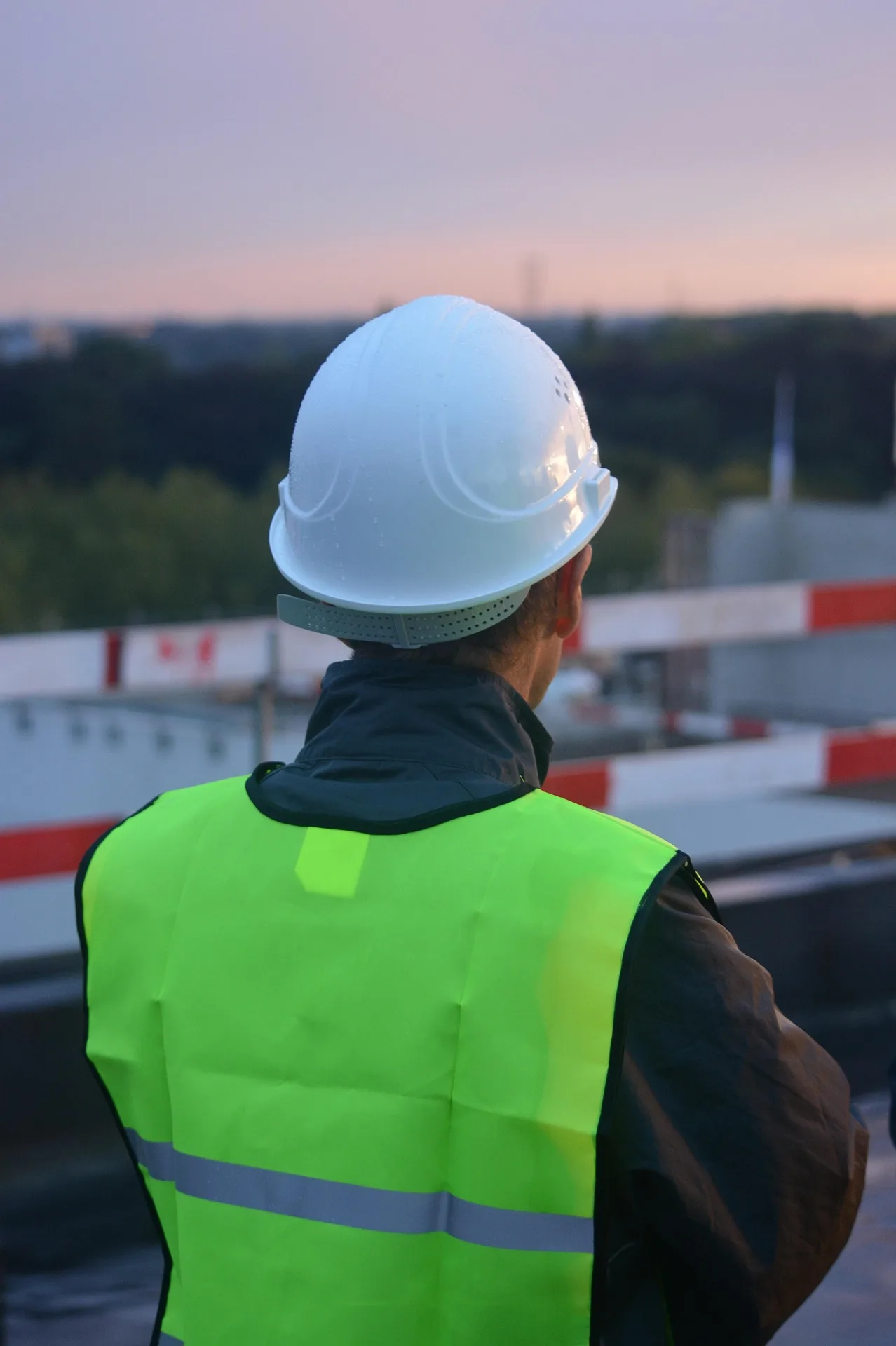 Two construction workers standing on an active building site under a bright, cloud-filled sky