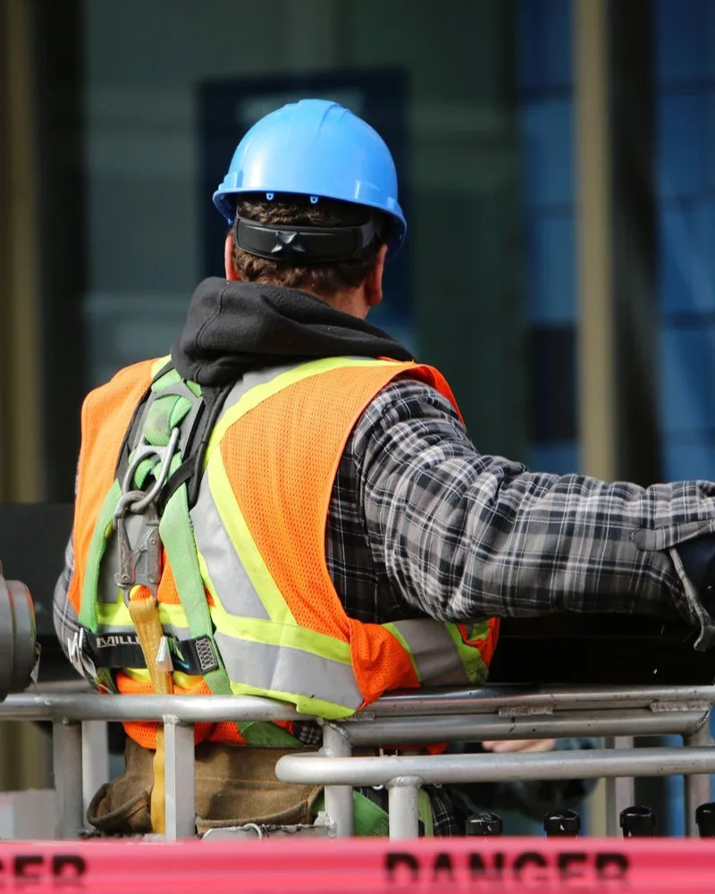 Two construction contractors in hard hats and safety gear installing an electrical panel outside a building site