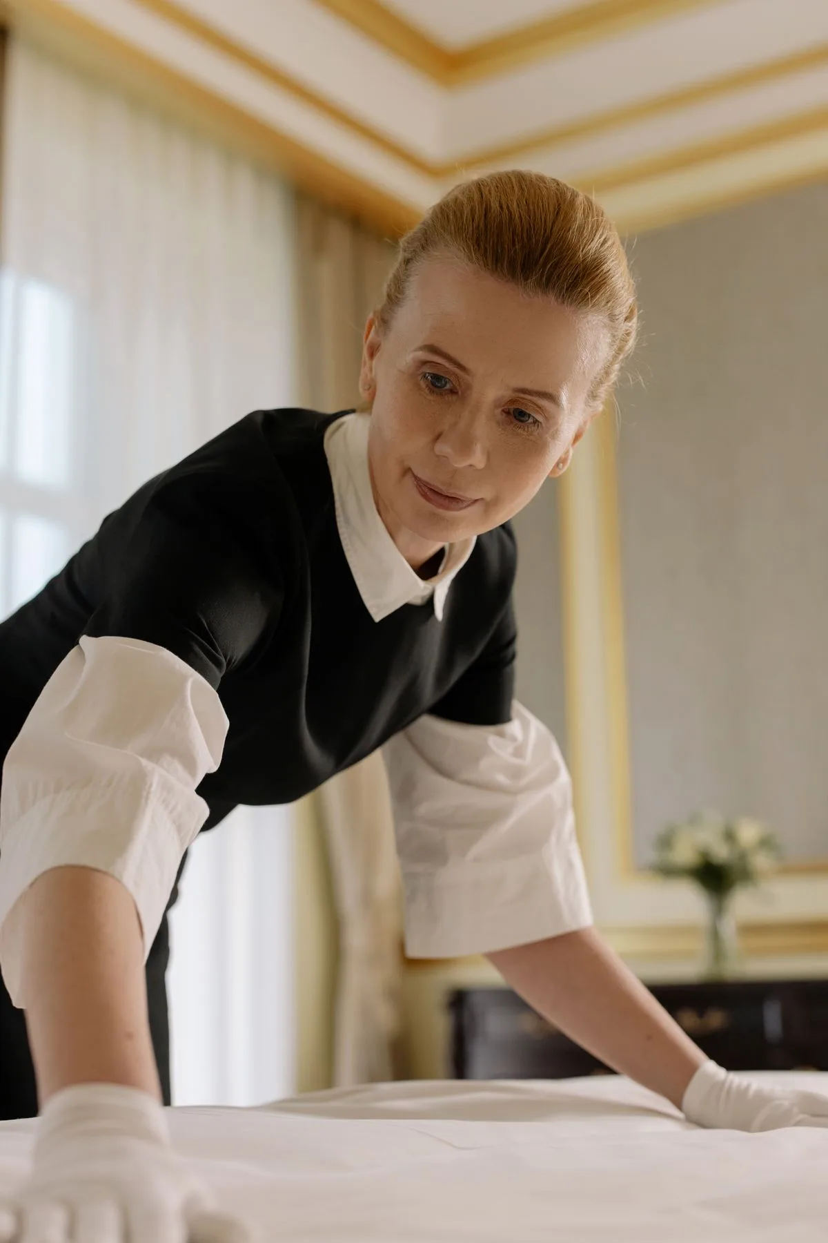 Hotel housekeeper in uniform making up a bed in an upscale guest room
