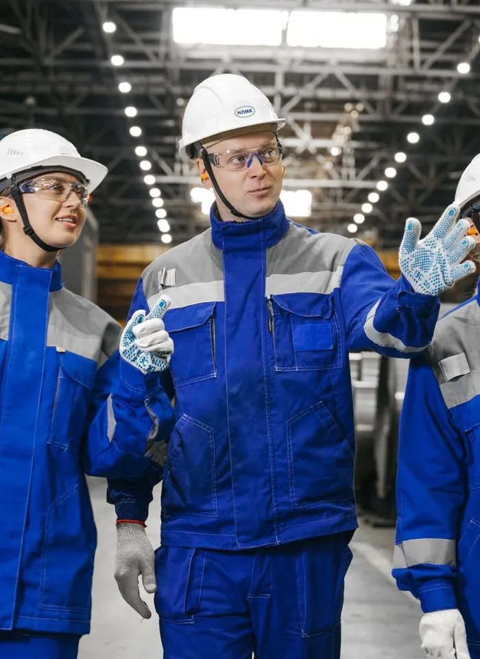 Group of manufacturing workers in hard hats and safety gear discussing on the floor of an industrial steel plant