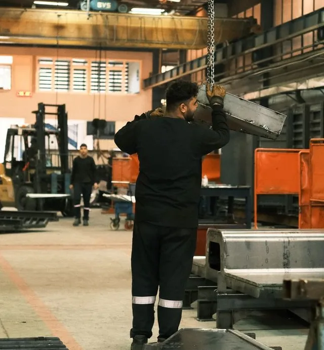 Manufacturing worker in protective gear guiding an overhead crane load on a plant floor