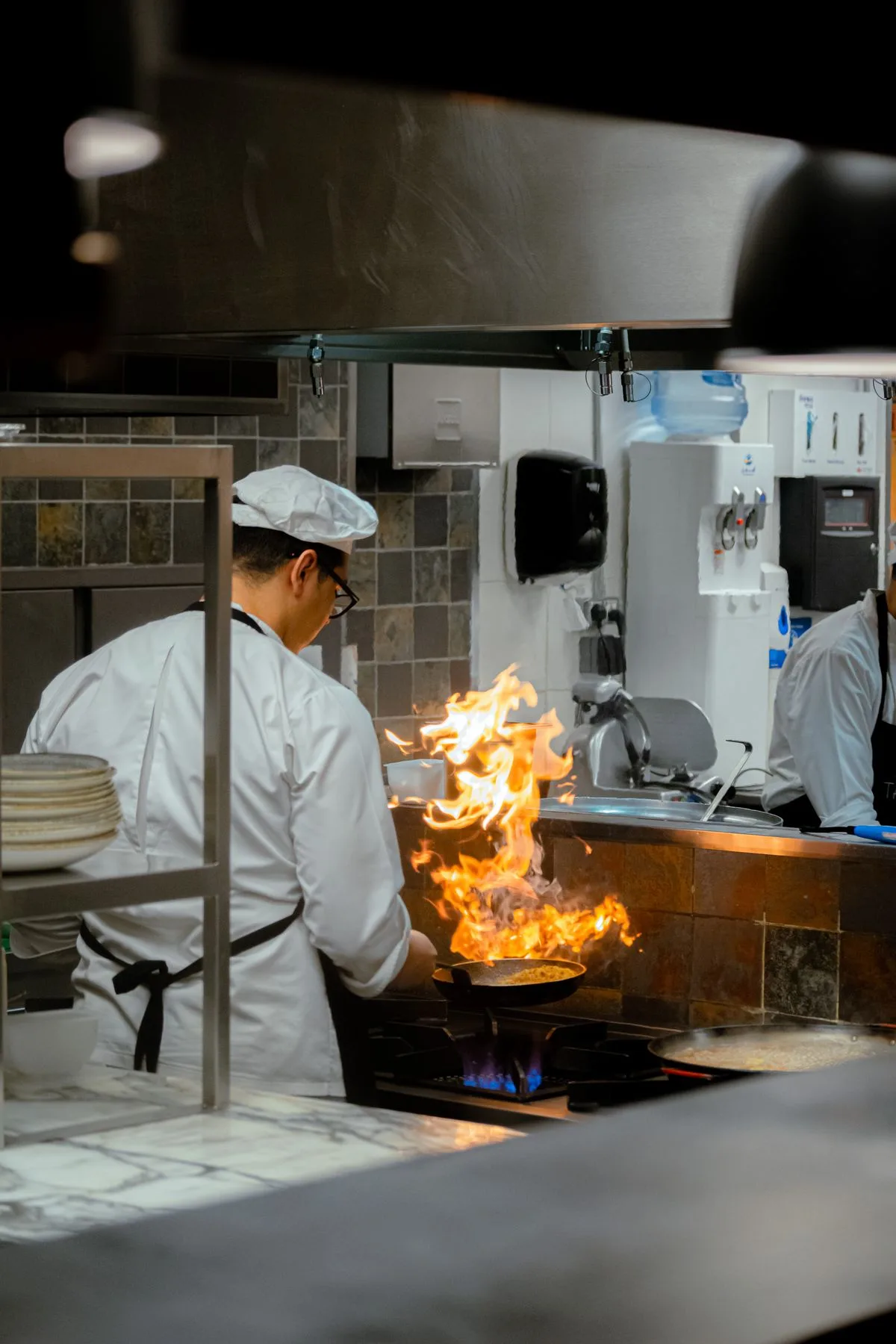 Restaurant chef searing food in a flaming pan in a busy commercial kitchen