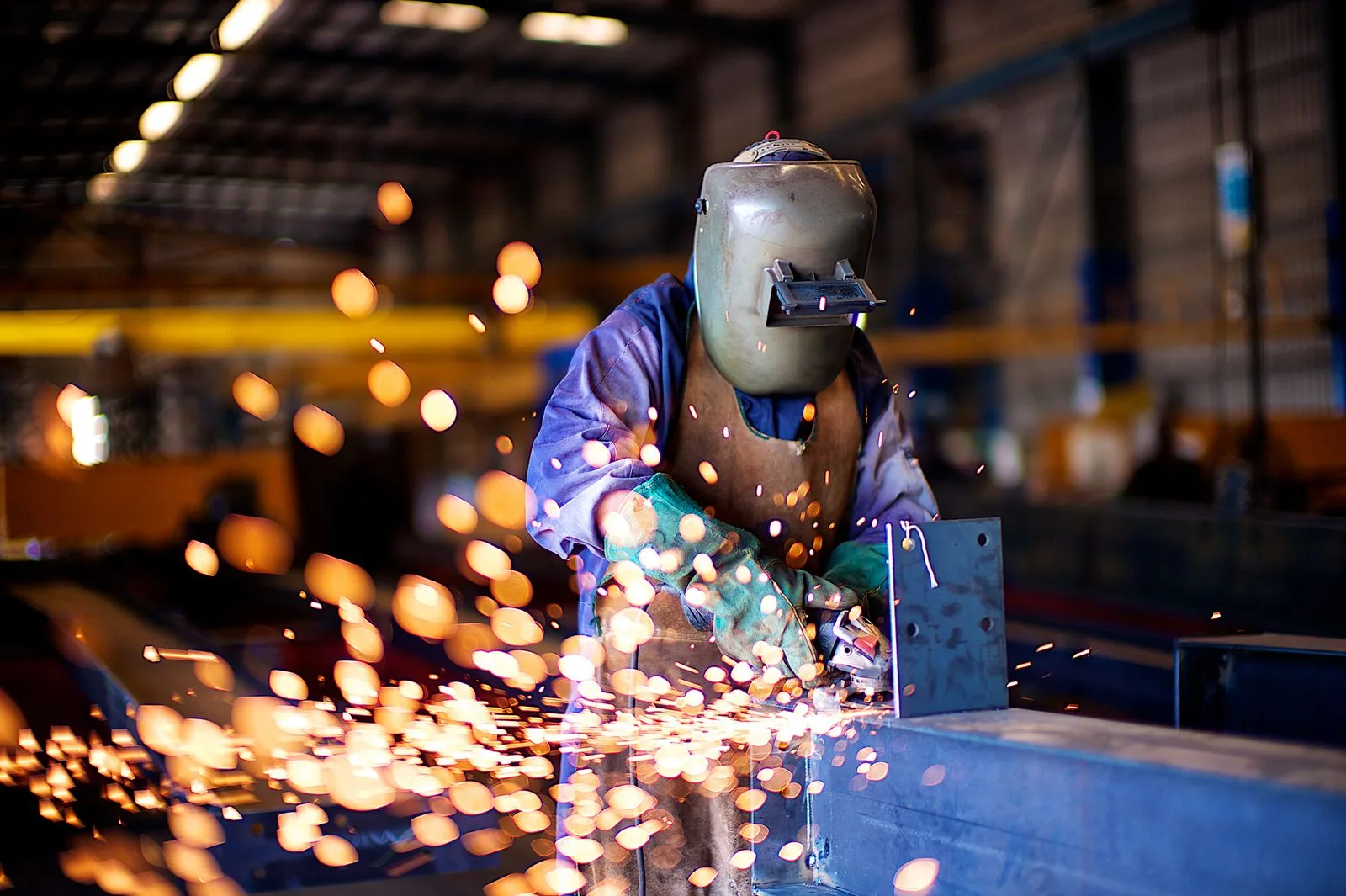 Fabrication shop worker in full protective gear welding metal, with sparks controlled at the workstation